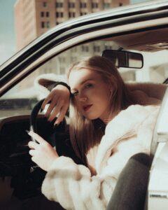 Woman sitting in a car wearing white fur coat